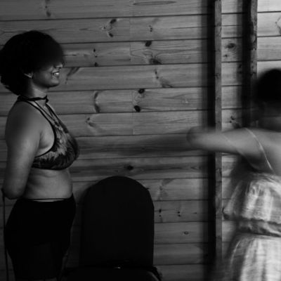 An out-of-focus shot in black and white of two female- presenting kinksters engaging in whipping.
