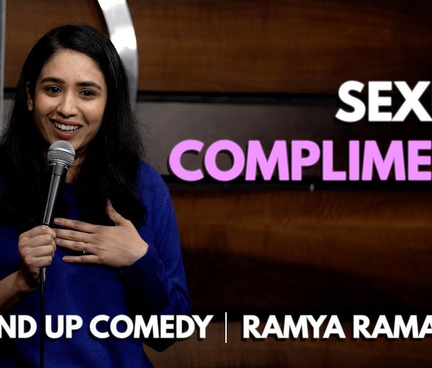Cover of YouTube video. Photo of Ramya Ramapriya on the left side of the image - she has long black hair and is smile. She is holding a mic and has her other hand on her chest. Text on the right side of the image reads, "Sexual Compliments" which is the title of the video. Across the bottom, the text reads, "Stand Up Comedy | Ramya Ramapriya