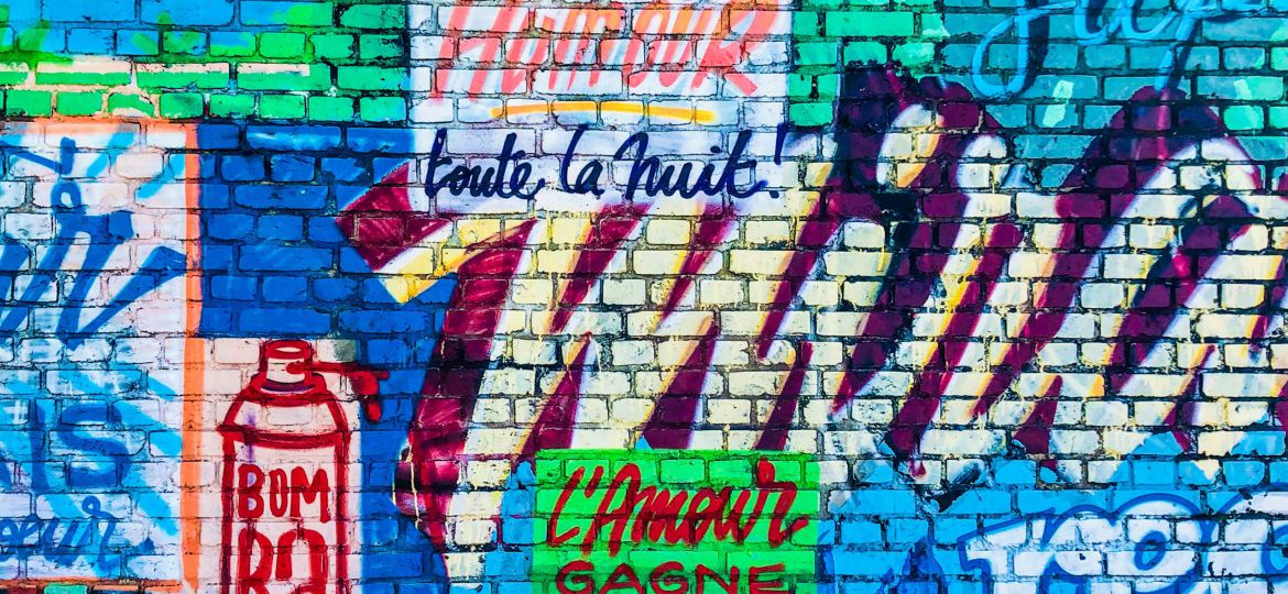 Close-up of a brick wall with heavy neon graffiti. The text, wherever present, is in French.