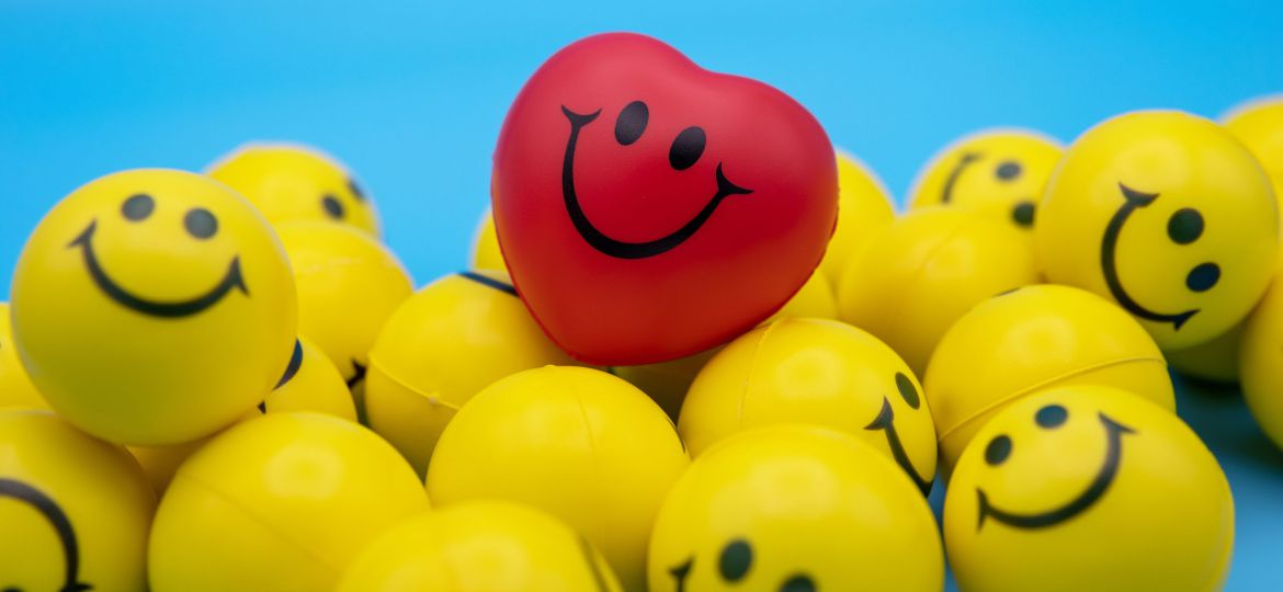 A red heart-shaped smiley ball kept on a pile of yellow smiley balls.