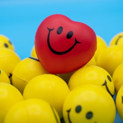 A red heart-shaped smiley ball kept on a pile of yellow smiley balls.