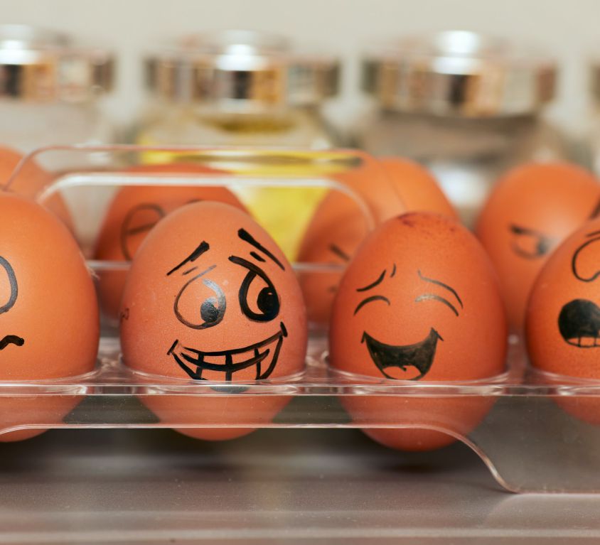A row of brown eggs with faces and different expressions painted on them with a black marker.