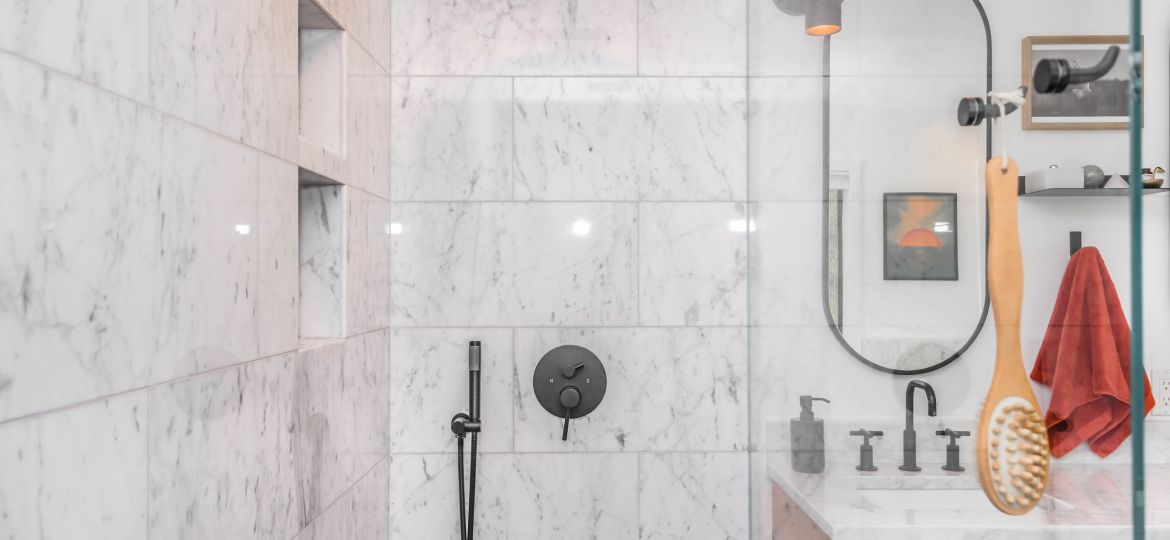 Shower cubicle with a black showerhead and textured white ceramic tiles. The basin with a mirror is also visible.