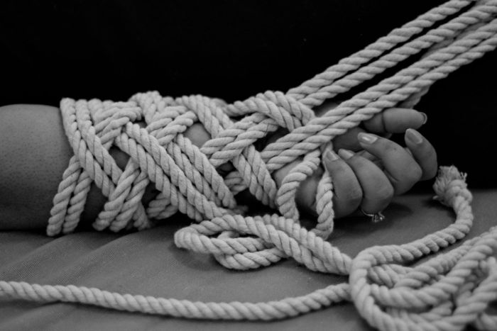 A black and white photo of hands tied by rope.