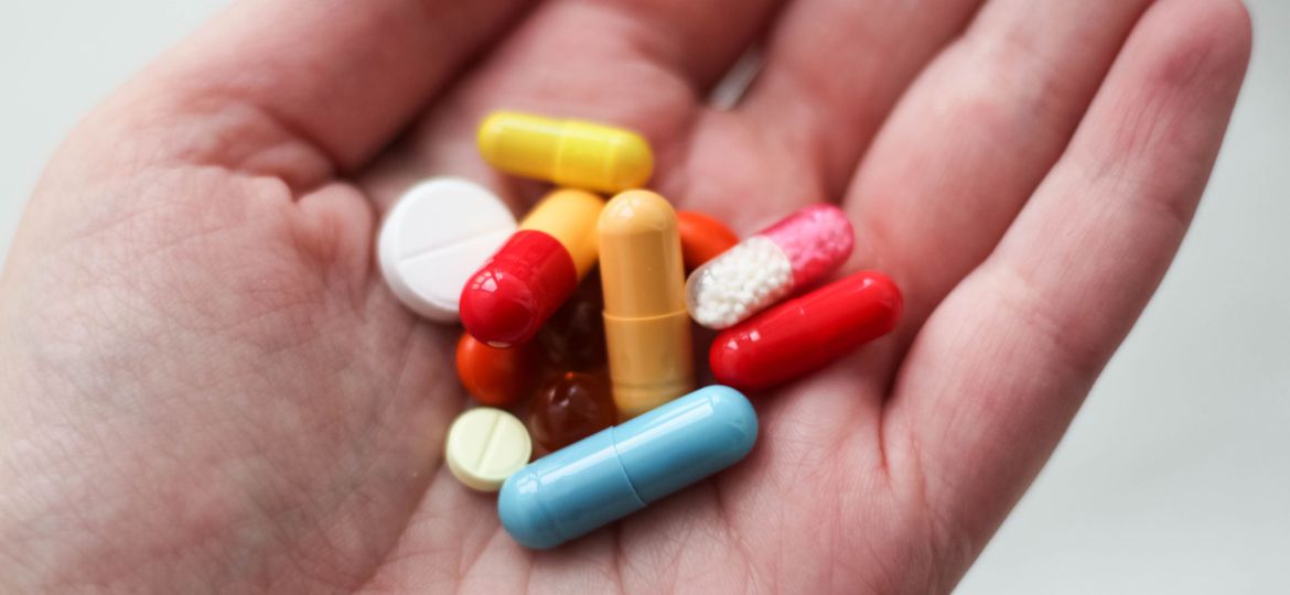 A close-up shot of an open palm with different kinds of pills, both tablets and capsules, on it.