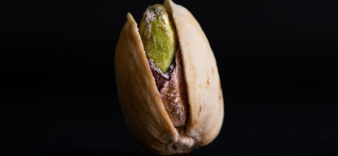 A single, slated pistachio kept upright on a black surface.