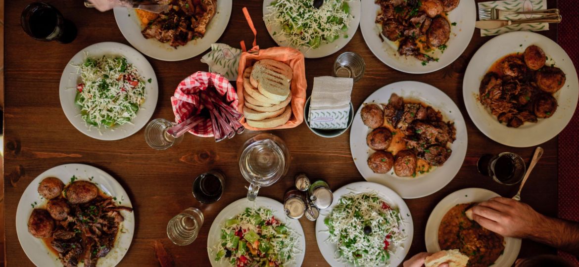 An overhead shot of a set table and people eating. There are white plates with different kinds of food and the individuals are towards the edges.