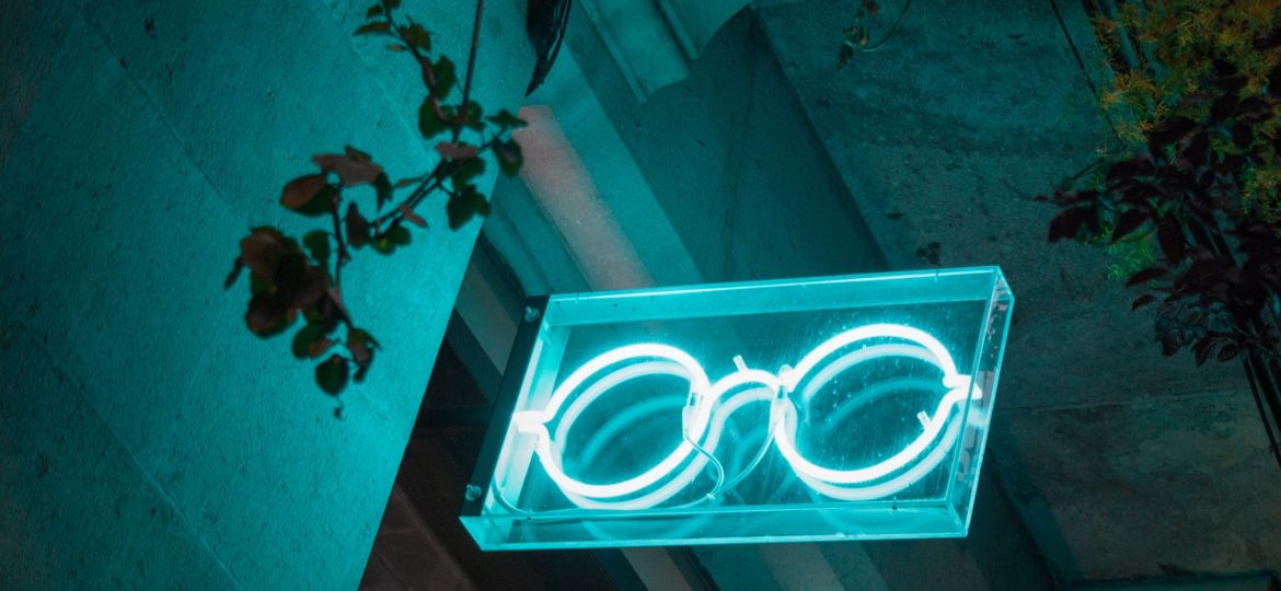 sea-green neon light signboard on a door showing white hippie glasses neon.