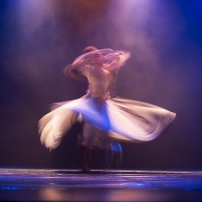 A blurred image of a woman in white long sleeve shirt with white scarf from a solo dance in a live show during Ramallah Contemporary Dance Festival.