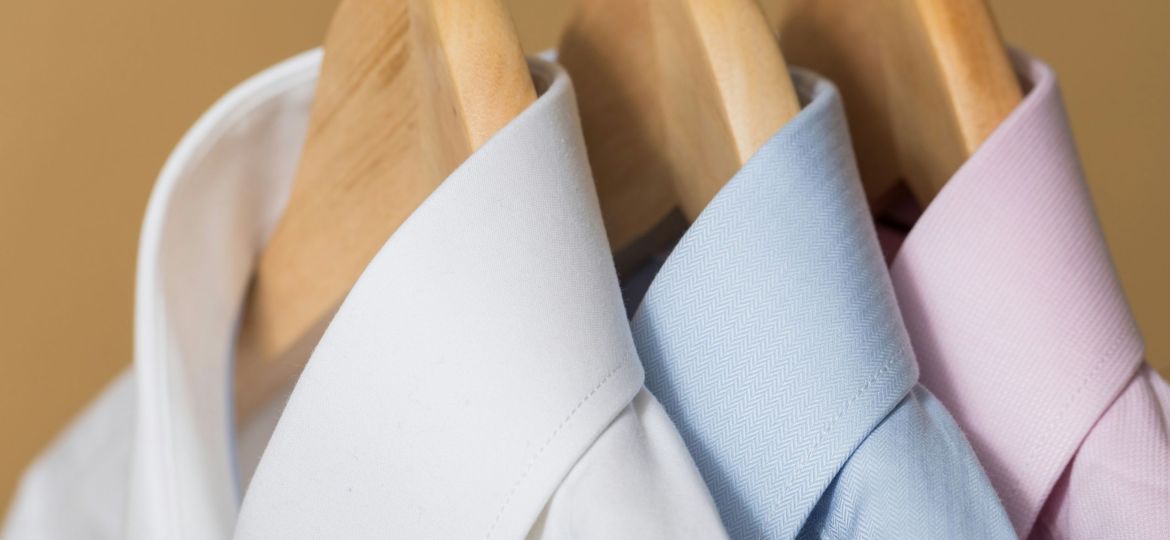 Closeup photo of the three formal shirts in white, blue and light pink hanged neatly