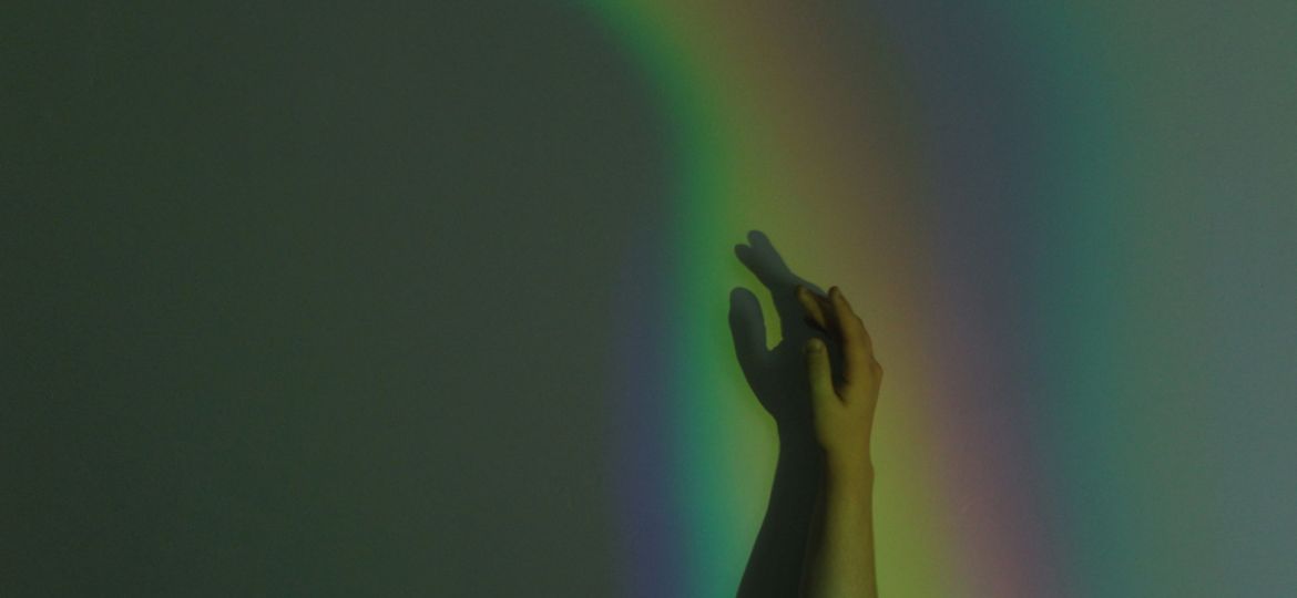 A person's hand reaches up, illuminated by a rainbow display projected onto it.