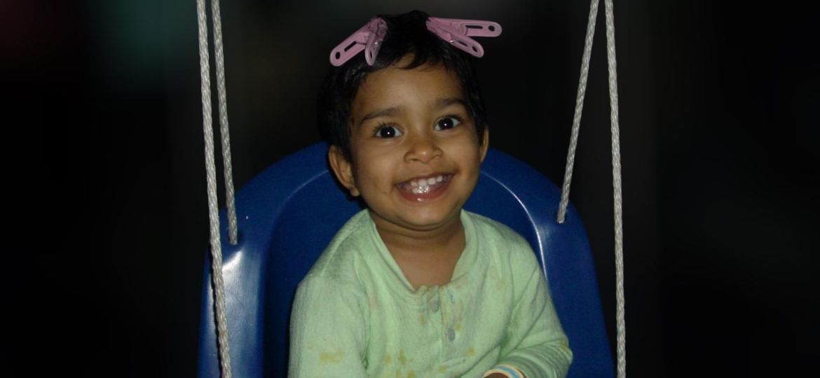 A little child smiling on a blue swing