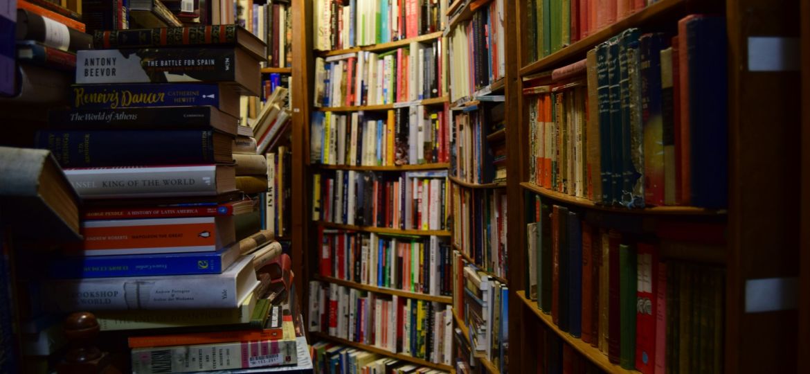 A dimly lit bookshelf corner with books stacked haphazardly