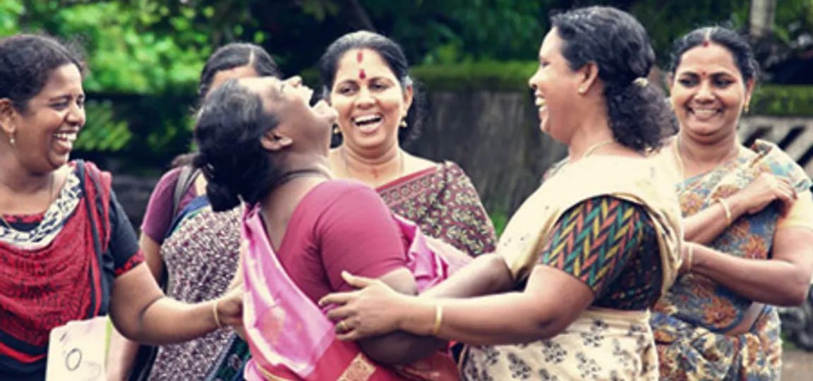A group of middle aged women from Kerala embracing each other and laughing joyously