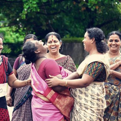 A group of middle aged women from Kerala embracing each other and laughing joyously