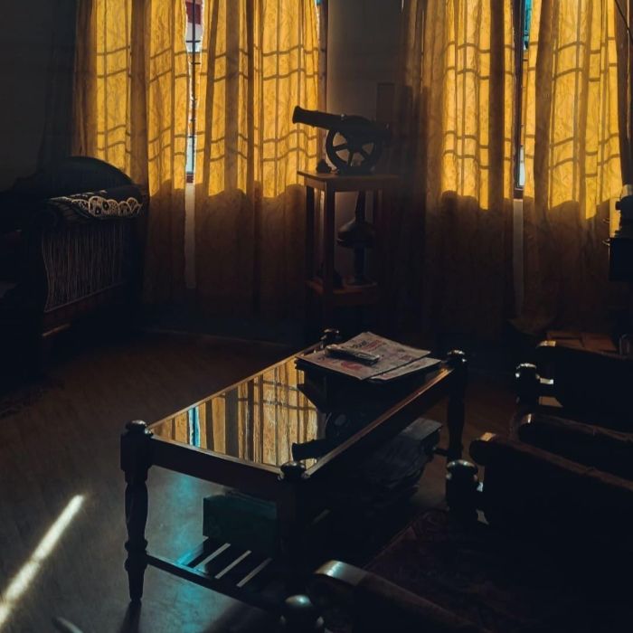 A living room photograph taken during the golden hour where the curtains are drawn in and the glass top of the centre table reflects the bright curtains