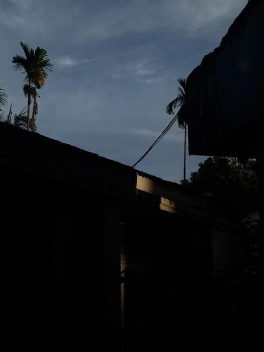 a phpto of the sky at dusk from a window. It overlooks a building in shadow and a betel nut tree