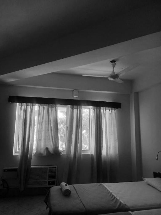 The quiet personal space of a neatly made bed and the sheer curtains drawn over the window